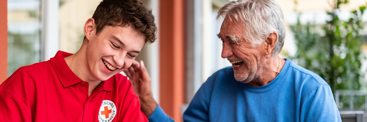 Senior hält einem jungen DRK-Mitarbeiter die Hand auf dessen Schulter