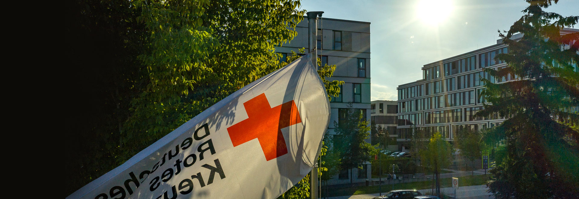 DRK-Fahne vor Baum und Gebäuden in der Abendsonne