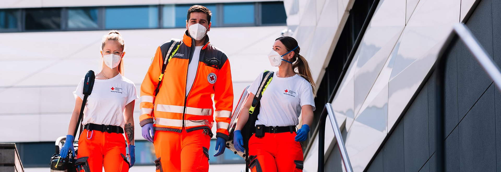 Zwei Rettungssanitäterinnen und ein Rettungssanitäter laufen eine Treppe herunter