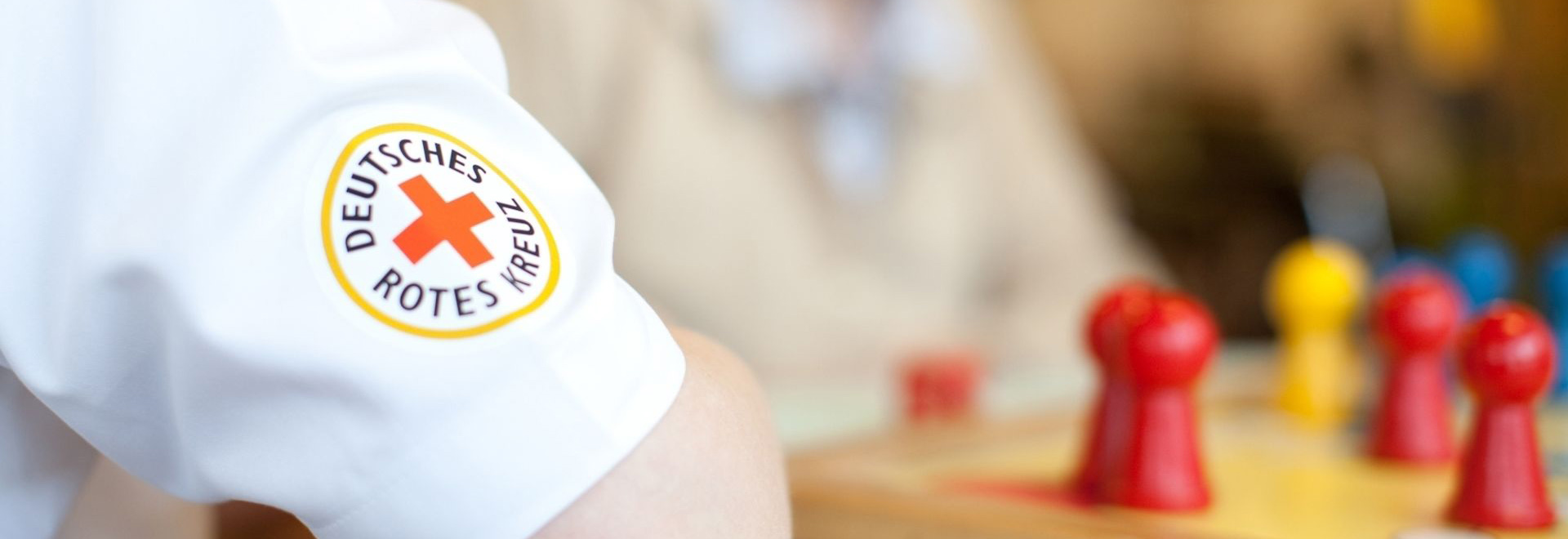 Ärmel mit DRK-Logo, im Hintergrund unscharfe Spielfiguren