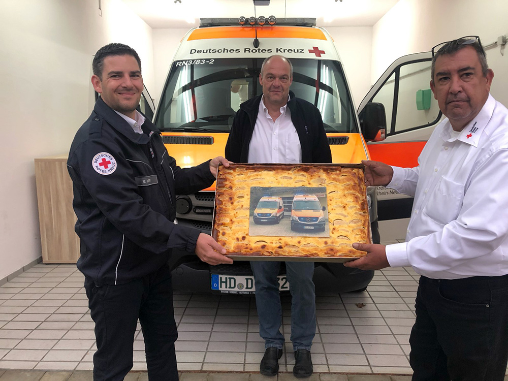 Zwei DRK-Mitarbeiter überreichen dem Standortleiter einen Blechkuchen