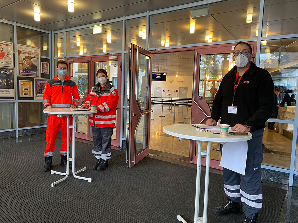 DRK-Mitarbeiter stehen für eine Beratung der Impfwilligen an Stehtischen bereit