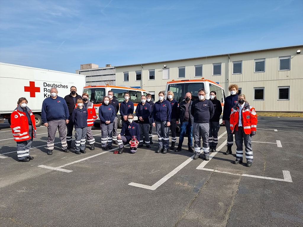 Gruppe von Ehrenamtlichen Helfern und DRK-Mitarbeitern vor DRK-Fahrzeugen