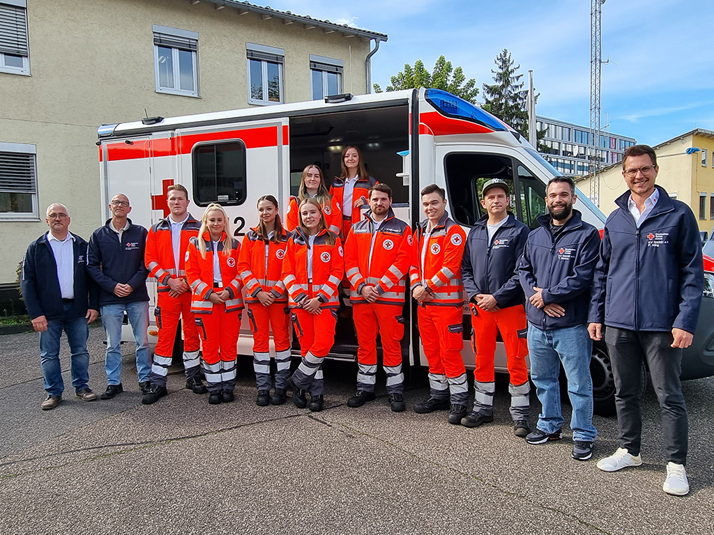Gruppenbild: 8 angehende NotfallsanitäterInnen vor einem Rettungswagen mit ihren Ausbildern