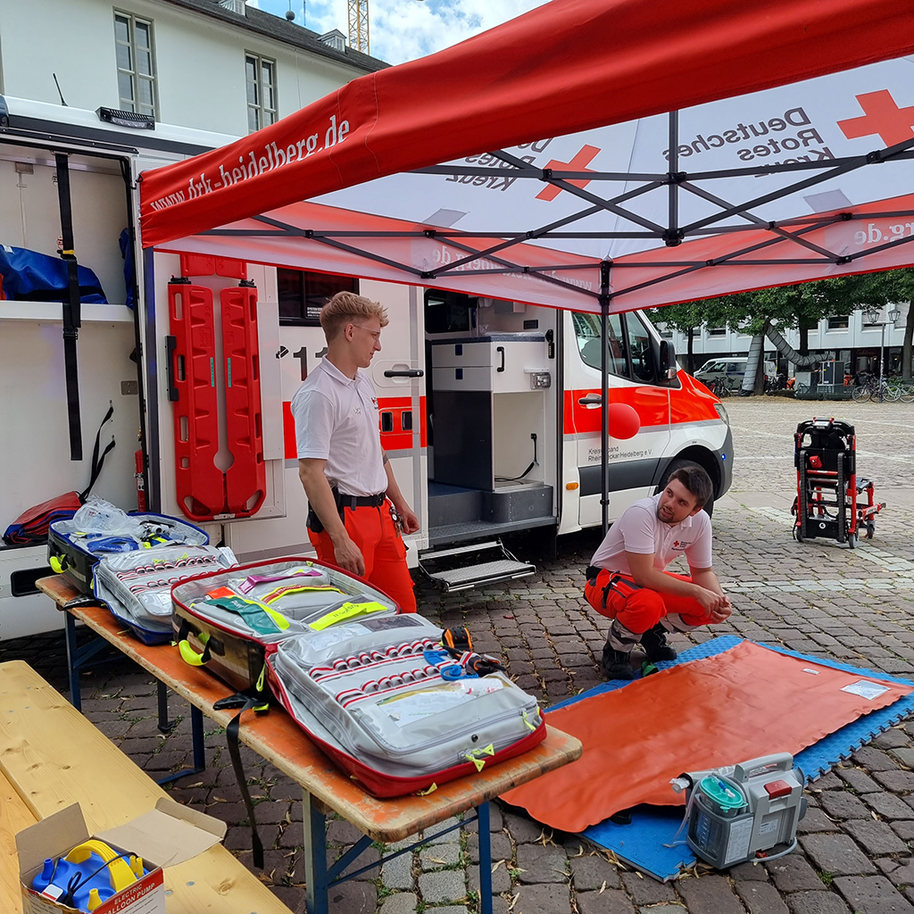 Zwei Sanitäter unter einem Sonnenschirm und mit Utensilien, um Erste Hilfe zu leisten