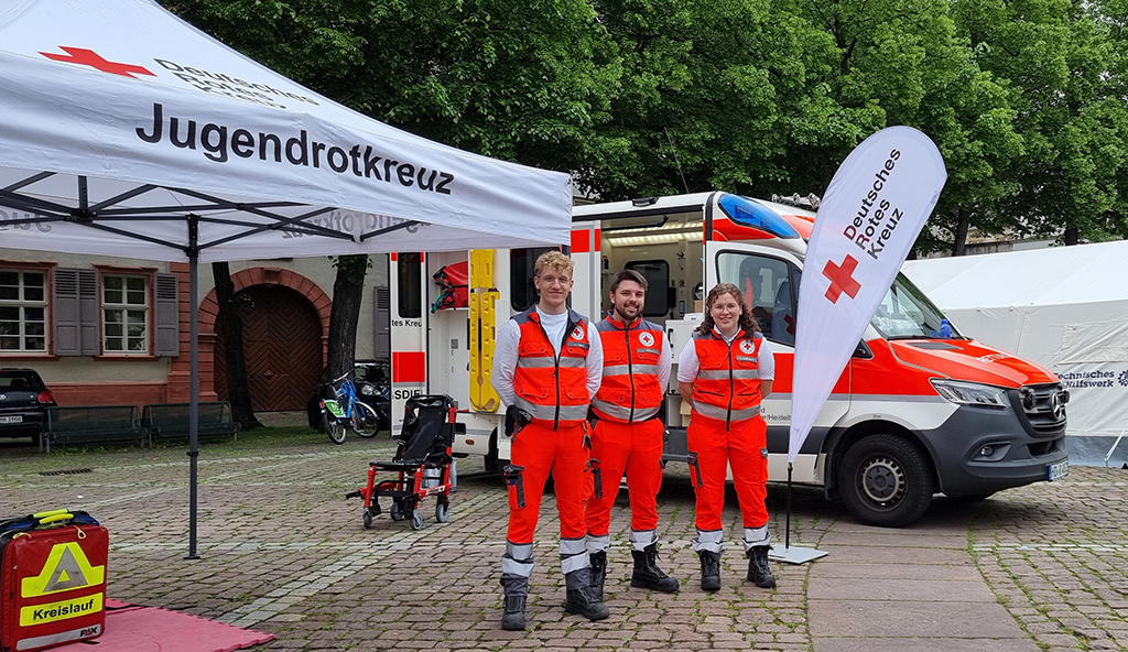 Drei DRK Notfallsanitäter/innen neben dem Medizin-Zelt und einem Rettungswagen