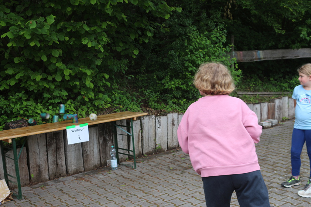 Mädchen wirft einen Ball beim Weitwurf auf eine Pyramide aus Blechdosen