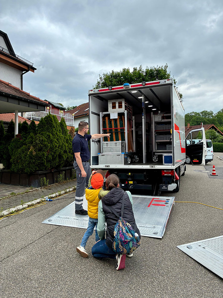 Eine Mutter schaut mit ihrem Kind in ein am Heck geöffnetes DRk-Fahrzeug des Bevölkerungsschutzes