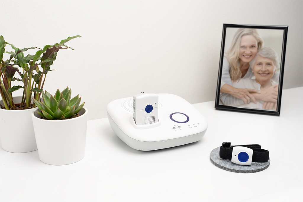 Basisstation für zu Hause mit handlichem Hausnotrufknopf, welcher wie eine Uhr am Handgelenk getragen werden kann.