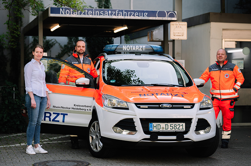 Drei Personen neben einem Einsatzfahrzeug