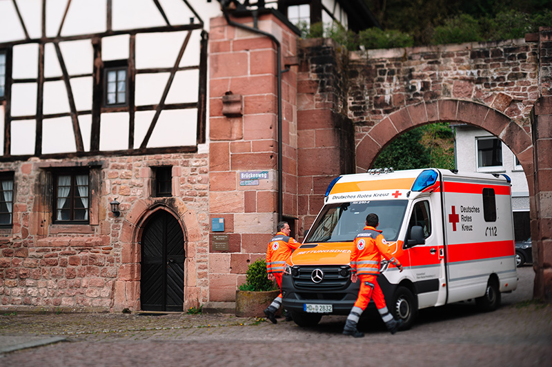 Rettungswagen und zwei Mitarbeiter neben einem alten Fachwerkgebäude