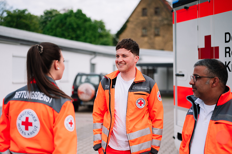 Drei Rettungssanitäter unterhalten sich auf dem Parkplatz der Rettungswache Walldorf