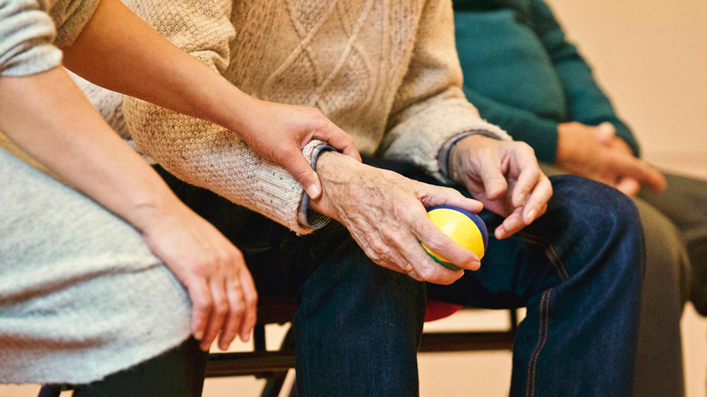 Frau hält das Handgelenk eines Seniors, der einen Ball in der Hand hat