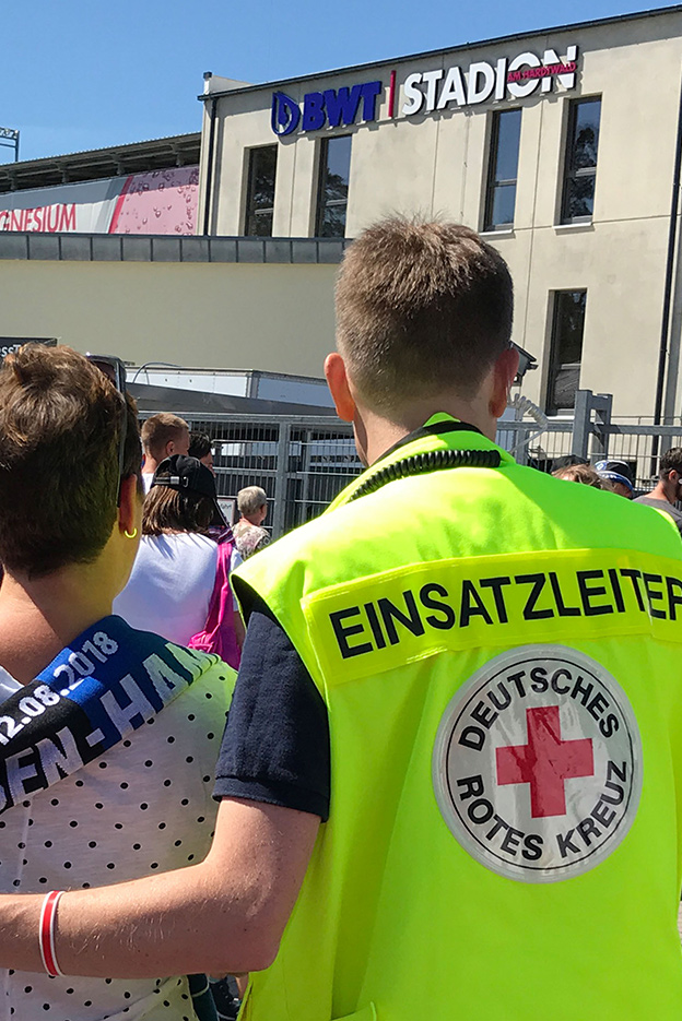DRK-Mitarbeiter mit einer Weste mit Aufschrift Einsatzleiter kümmert sich um eine Frau bei einer Veranstaltung