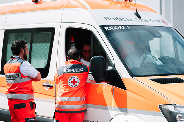 Zwei Rettungssanitäter stehen neben einer Rettungswagen und unterhalten sich mit einem anderen Rettungssanitäter, der im Fahrzeug sitzt