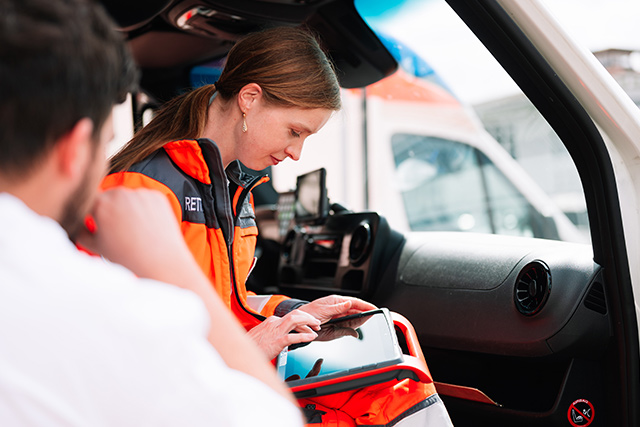 DRK-Mitarbeiter sitzt im Rettungswagen und notiert etwas in ihr Tablet